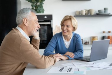 Modern mutfakta oturan emekli bir çiftin portresi. Kocası telefonla konuşuyor. Finansal sorunları çözmek. Fatura belgeleri. Aile bütçesi planlamak. Masraflar hesaplanıyor