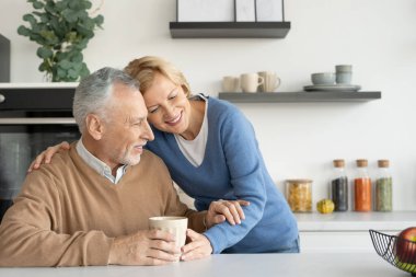 Gülen ve sevecen emekli bir eş kocasına sarılıyor. Sabah kahvesi ya da çay içmek. Ev rahatlığı. Sonsuza dek aşk konsepti. Birlikte mutlu olmak.