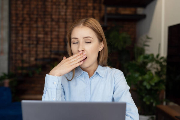 Портрет уставшей женщины, зевающей перед ноутбуком. Перегруженная концепция фрилансера. Работаю из дома. Концепция выгорания рабочих мест. Ленивая рабочая леди