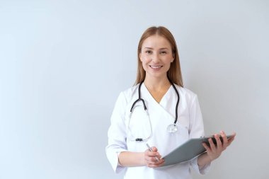 Tıbbi üniforma giyen pratisyen, steteskopla fotokopi alanının arka planına bakıyor. Kadın doktor hastanın tıbbi kayıtlarını tutuyor, kameraya bakıyor, sırıtıyor. Sağlık hizmeti kavramı