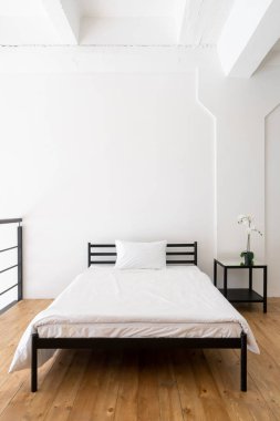 Temiz beyaz çarşafları olan güzel bir yatak odası iç tasarımı. Minimalist ev dekorasyonları. Çiçekli komodin. Sabahın doğal ışığı