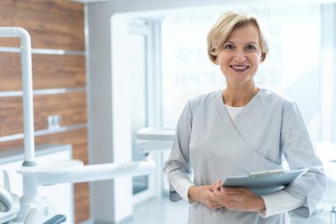 Çağdaş hastane ofisinde duran dosyasıyla gülümseyen stomatolojistin portresi. Sağlık sigortası konsepti. Tıbbi personel. Diş sağlığı sektörü