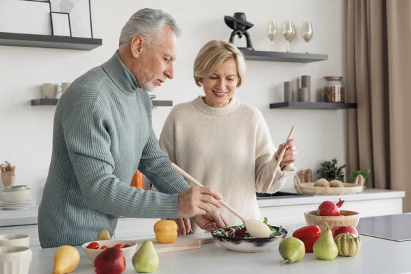 一緒にサラダを作る笑顔のシニアカップルの肖像画 家の快適さ 明るいキッチンで一緒に昼食を調理するプロセス 健康的なライフスタイル — ストック写真