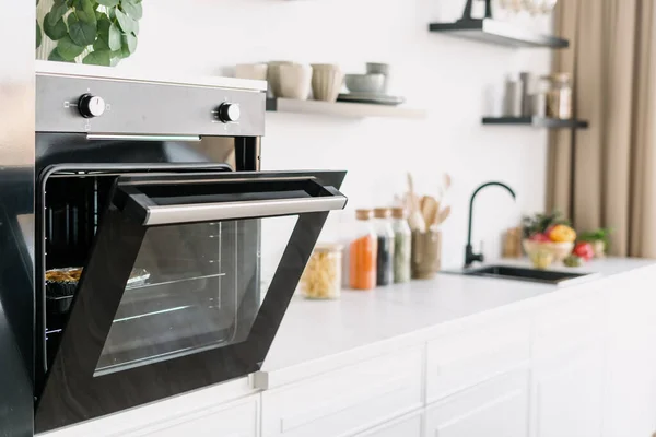 Side view of black oven with open door in modern Scandinavian studio style. Contemporary white wood furniture and kitchenware. Cozy place for cooking