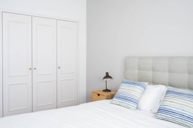 Geniş gardırobu, rahat yatağı ve elektrikli lambası olan ahşap komodinlerin ya da sehpaların üzerindeki parlak otel odasının yan görüntüsü. Yatak odasındaki dolapta. Modern iç tasarımı olan bir daire.