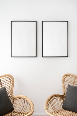 Model konseptleri. Hasır rattan koltukların üzerinde beyaz duvarda asılı boş arkaplan olan iki boş uzay resim çerçevesinin dikey görüntüsü. Sıcak boho iç mekan elementi