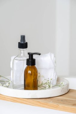 Dikey sabun makinesi, vücut losyonu ve cam şişedeki doğal organik kozmetik ürünleri parlak banyoda beyaz pamuk havluya yakın duruyor. Cilt bakımı kavramı