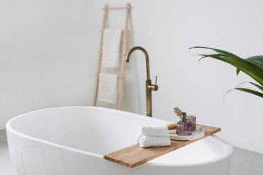 Temiz ve temiz havlular, küvetin üstündeki ahşap rafta. Çağdaş tasarımla aydınlık banyo iç mimarisi unsuru. Modern bir evde ya da lüks bir otelde ev dekorasyonu.
