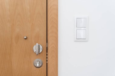 Tadilattan sonra modern dairenin duvarında kapalı ahşap kapı ve ışık düğmesi var. Güvenlik ve rahatlık kavramı. Minimalist ev iç tasarımı