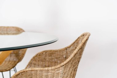 Boho Style Room 'daki cam yemek masasının yanındaki ahşap sandalyeyi kapat. Rahat koltuklar, rahat evlerde beyaz fotokopi duvarına karşı duran doğal malzemeler.