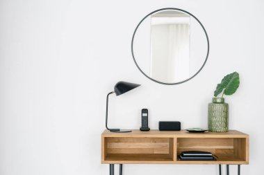 Çatı katı iç tasarım tarzıyla modern giriş salonu dairesi. Lamba, kablosuz telefon kablosuz istasyonda ve masa dekoru yuvarlak aynanın altında. Salondaki ahşap mobilyalar.