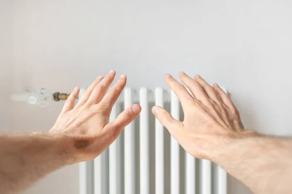 POV man reach hands to warmth heating radiator in cold room. Heat supply in residential buildings, growing utility bill prices and disconnection from energy systems concept