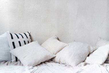 Yastıklar ve yastıklar buruşuk yatağın üzerinde kopya alanı olan dokulu duvarlara karşı. Açık renk yatak odalı iç mekan doğal tekstil döşeme ve boş arka planla bohem şıklığında.