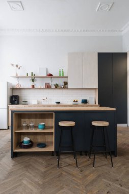 Lüks mobilyalar, ahşap dolaplar, tezgah ve ev aletleriyle modern mutfağın dikey görüntüsü. Çatı katı tarzı iç tasarımı olan bir evde, yemek masasının yanındaki bar sandalyeleri.
