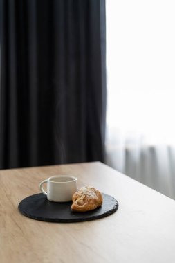 Kahve molası zamanı. Evde sabah kavramı. Aromatik kapuçino bardağını ahşap masada ev yapımı taze kruvasanla kaplayın. Siyah fotokopi arkaplanına karşı. Bardağın üstünde buhar.