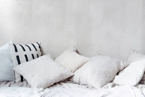 Yastıklar ve yastıklar buruşuk yatağın üzerinde kopya alanı olan dokulu duvarlara karşı. Açık renk yatak odalı iç mekan doğal tekstil döşeme ve boş arka planla bohem şıklığında.