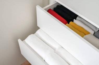 Beyaz komodinin içinde düzgünce katlanan çeşitli kıyafetlerin yüksek görünümü. Kişisel soyunma odası. Beyaz tonlarda çağdaş oda iç tasarımı. Organizasyon alanı