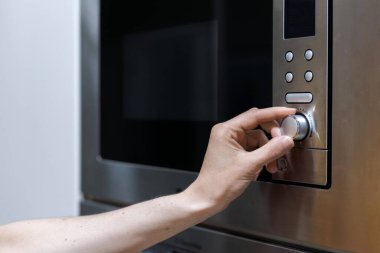 Mikrodalga fırın topuzunu çeviren birinin el görüntüsü. Ev aletleri. Akşam yemeğini hazırlıyorum. Zaman ve sıcaklığı mikrodalgada ayarlama işlemi. Yemek zamanı.