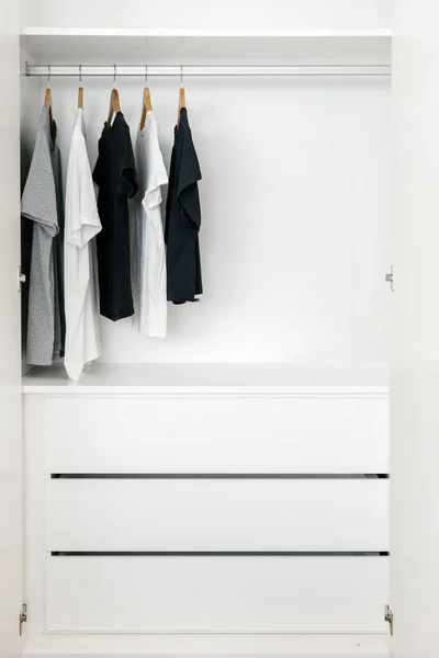 Personal dressing room with variety of T-shirts hanging on racks. Contemporary room interior design in white tones. Fashionable clothes. Organizational space