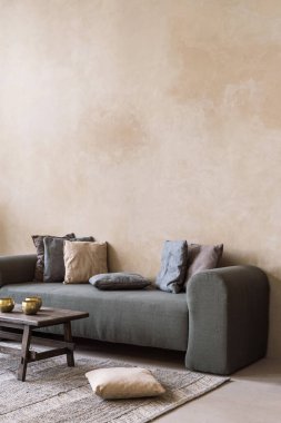 Yastıklı, dikey yeşil kanepe, oturma odasındaki bej fotokopi duvarının karşısında duruyor. Tibet kâseleriyle eski kırsal kahve masası rahat hygge apartmanında kanepeye yaslanmış.