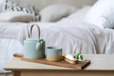 Parlak yatak odasının iç kısımları bohem şıklığında. Kahve masasındaki servis tepsisine çay, çaydanlık ve ekini kapatın. Arka planda bulanık yatağa karşı kahvaltı