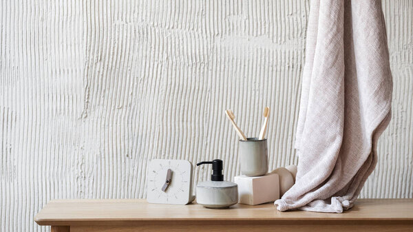 Wooden shelf in bathroom with modern alarm clock, soap dispenser and bamboo toothbrush for dental care in ceramic cup close to fresh clean bath towel. Selfcare at morning and beauty routine concept