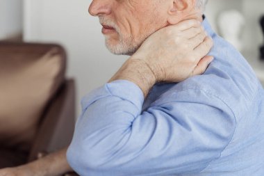 Health issues concept. Cropped view of sick mature aged man with neck pain. Pensioner touching his inflamed muscle or pinched nerve on shoulder