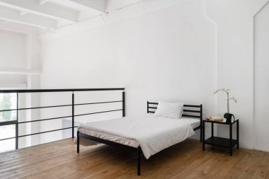 İkinci kattaki temiz beyaz çarşaflı, sade yatak odası dekorasyonunun yan görüntüsü. Çiçekli komodin. Çok katlı daireler.