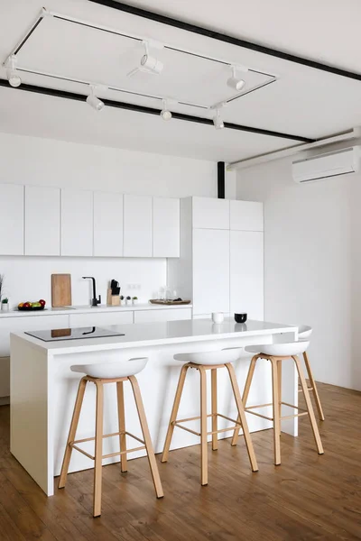 Side view of contemporary kitchen interior design in Nordic style with bar chairs. Spacious and bright apartment. Kitchen appliances and stylish white furniture