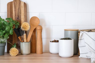 Kaplarda bitki çayı ve ahşap masadaki çevre dostu mutfak gereçleri. Ev rahatlığı. Mutfakta organizasyon alanı var. Çanak çömlek takımı