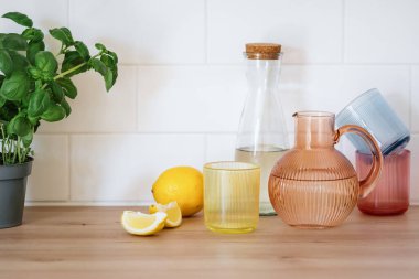 İçecekler için renkli cam eşyalar. Limonata ya da ahşap tezgah ya da mutfak masasında limon ve fesleğene yakın su standı için şişe, sürahi ve cam. Antioksidan, detoks ve içecek konsepti