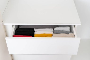 Giysi deposu dairede. Dolabın açık çekmecesinde düzenlenmiş katlanmış renkli kıyafetlerin yüksek açılı görüntüsü. Dolap ve tuvaletteki düzenlilik kavramı