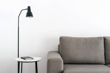 Not defteri ve lamba beyaz stil odasındaki kanepenin yanındaki komodinin üzerinde. Minimalist ve çağdaş iç tasarım. Ev rahatlığı. Tadilattan sonra geniş bir oda