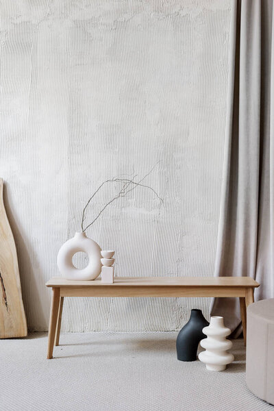 Cropped view of ceramic vases with branches and wooden board in room with beige textured walls. Still life composition. Cozy flat design idea