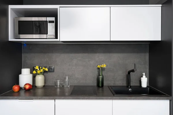 Nordic compact kitchen interior design in black and white tones. Cozy place for cooking. Kitchenware and fruits. Home comfort. Luxury flat for rent