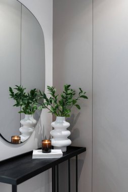 Modern mobilyaları ve oturma odasında ya da yatak odasında dekorasyonu olan rahat bir daire. Seramik vazoda bitki bulunan ahşap masa, aynanın yanında duran kağıt üzerinde mum, gardıroba karşı.