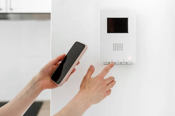 Concept of mobile app for smart home system. Cropped view of woman with modern smartphone touch to control panel, open front door, checking security and managing wireless devices in apartment