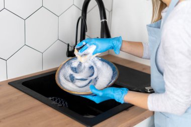 Önlüklü kadın ve eldiven yıkama tabağı. Modern mutfakta lavabo musluğunu temizleyen mutfak gereçleri. Ev hanımı konsepti. Temizlik işçisi