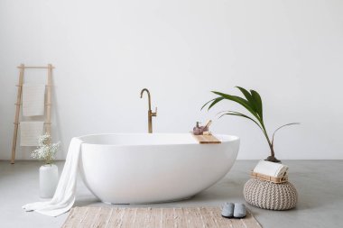 Minimalistik banyo içi beyaz modern küvet. Rahat bir dairede ya da otel odasında klasik tasarımı olan porselen bir küvet. Spa merkezinde ev dekorasyonu ve ev bitkisi