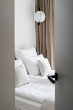 Otel odasını açık kapıdan görmek, beyaz yatak, rahat oda, hipoalerjenik yastıklar, konfor fikri, yatak odası iç tasarımı.