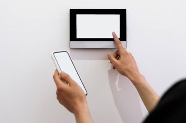 Akıllı ev aletlerini kontrol eden kadın, modern akıllı telefonunu kullansın. Oturma odasındaki duvara kadın eli dokunmatik ekran paneli yerleştirilmiş. Boş uzay görüntüsü, dijital teknoloji