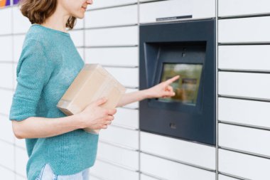 Concept of contactless and smart delivery. Happy woman with parcel confirm receiving package standing near automatic post terminal outdoors. Idea of modern shipping and logistics
