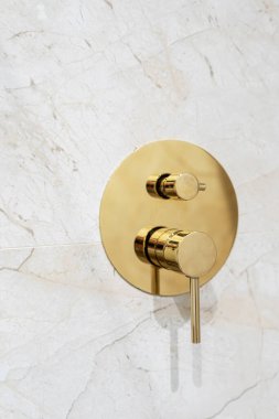 Altın metal su karıştırıcısının dikey görüntüsü. Duş odasında yeni, parlak, lüks tesisatı yakın çekim. Musluk duvardaki mermer fayanslara karşı. Klasik tarzda bir dairede banyo. Reklam kavramı