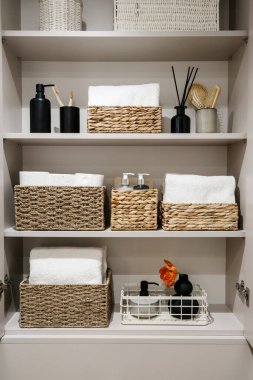 Ev eşyaları, tuvalet kağıdı ruloları, beyaz banyo havluları ve gardıroptaki tuvalet düzeninde raflarda kozmetik şişeler. Yatak, keten, ev parfümleri ve katlanmış bornozlar.