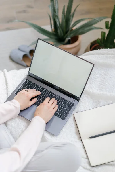 Concept of blogging, e-learning and remotely work at home. Cropped vertical view of copywriter or student sitting on bed, using modern laptop with blank screen. Woman blogger in bohemian bedroom