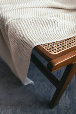 Beyaz örülmüş yumuşak battaniyenin yakın çekimi yeni bir rattan sandalyeyi örtüyor. Ahşap sandalyede bohem tarzında uzanan rahat bir ekose. Oturma odasının iç dizaynı.