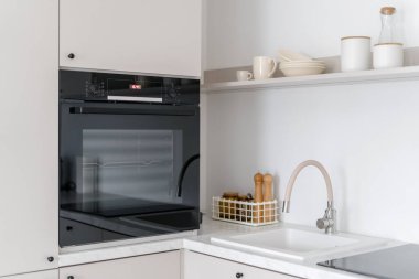 Çağdaş siyah fırının, lavabonun ve mutfak eşyalarının yan görüntüsü. Beyaz ahşap mobilyalar, dekoratif eşyalar. Fırın konsepti. Yemek yapmak için rahat bir yer.