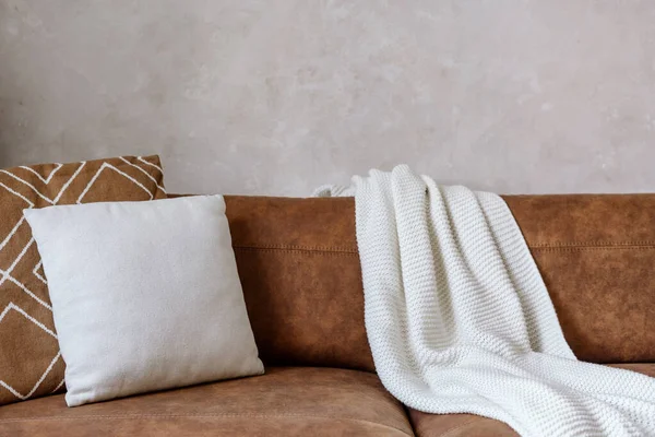 Closeup of brown eco leather couch with soft cushions and knitted white blanket near wall in room indoor. Modern design of living room, dry cleaning furniture concepts