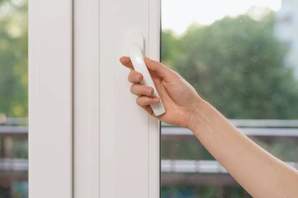 Cropped view of woman hand open plastic window in living room. Female hold handle, closed double glazed pvc balcony door, protect bedroom and insulate apartment from outdoors noise
