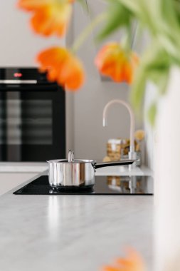 Seçici odaklanma, indüksiyon tenceresi üzerinde parlak metal bir tencereye odaklanma. Sağlıklı yiyecekler cam seramik ocakta pişiyor. Arka planda bulanık fırına karşı. Modern mutfakta mutfak gereçleri, dikey çekim